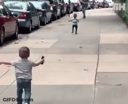 A Little Boy Is Walking Down A Sidewalk While Holding A Cell Phone In His Hand . GIF