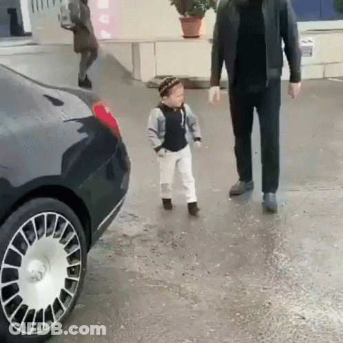 A Little Boy Is Walking Next To A Man In A Black Jacket . GIF