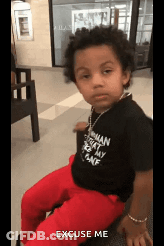 A Little Boy Wearing A Black Shirt That Says Excuse Me Is Sitting On A Chair GIF