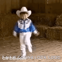 A Little Boy Wearing A Cowboy Hat And A Blue Jacket Is Walking On A Sidewalk . GIF