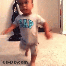A Little Boy Wearing A Gap Shirt Is Walking On A Carpet . GIF