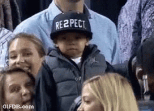 A Little Boy Wearing A Hat That Says Respect Is Sitting In The Stands . GIF