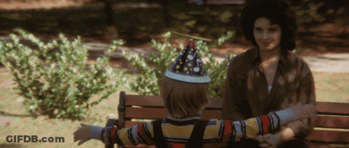 A Little Boy Wearing A Party Hat Sits On A Bench GIF