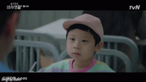 A Little Boy Wearing A Pink Hat And A Colorful Shirt Is Sitting In A Hospital Bed . GIF