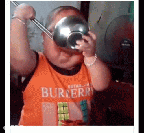 A Little Boy Wearing An Orange Shirt Is Holding A Bowl Over His Head . GIF