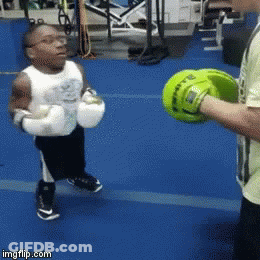 A Little Boy Wearing Boxing Gloves Is Being Taught How To Box By A Man GIF