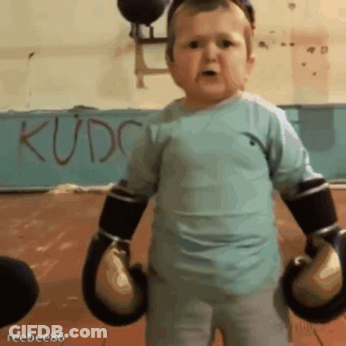 A Little Boy Wearing Boxing Gloves Is Standing In Front Of A Wall That Says Kudc GIF