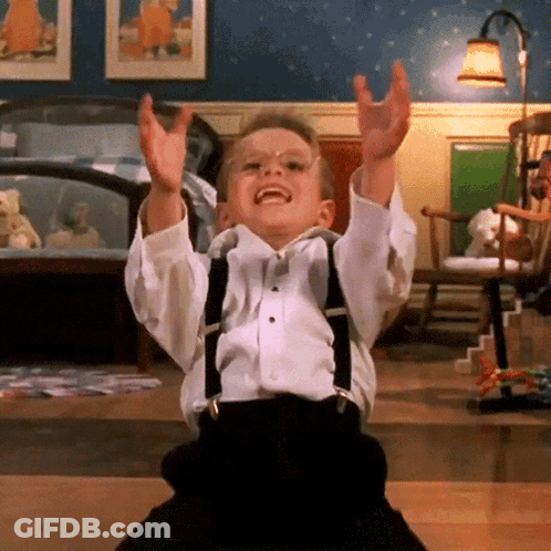 A Little Boy Wearing Suspenders And A Bow Tie Is Sitting On The Floor With His Arms In The Air GIF