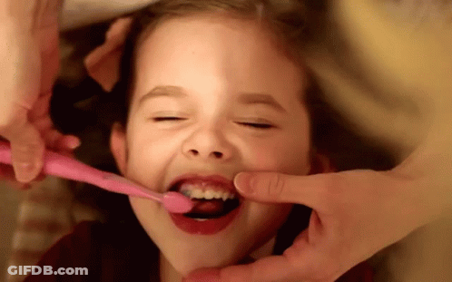 A Little Girl Brushing Her Teeth With A Pink Brush GIF
