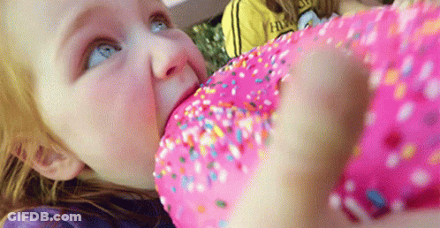 A Little Girl Eating A Pink Donut With Sprinkles GIF