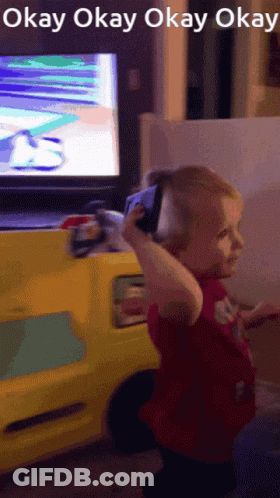 A Little Girl Holding A Cell Phone In Front Of A Tv Screen That Says Okay Okay Okay Okay GIF