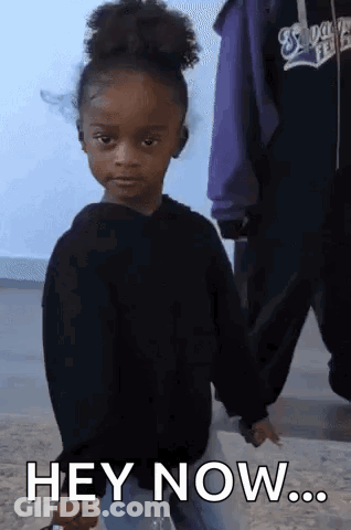 A Little Girl In A Black Sweater Is Holding A Bottle And Says Hey Now GIF