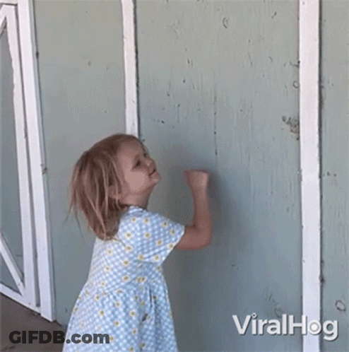 A Little Girl In A Blue And Yellow Dress Is Standing In Front Of A Wall . GIF