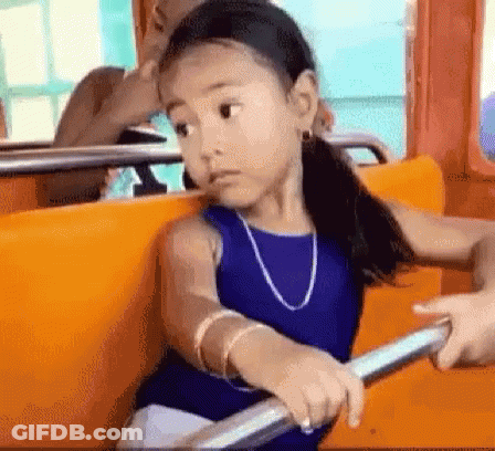 A Little Girl In A Blue Dress Is Sitting On A Bus Holding Onto A Railing . GIF