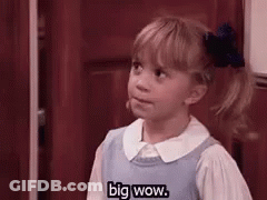 A Little Girl In A Blue Dress Is Standing In Front Of A Door . GIF
