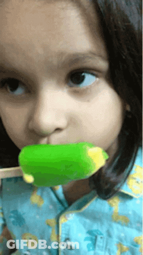 A Little Girl In A Blue Shirt Is Eating A Green Ice Cream Bar GIF