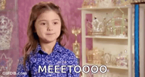 A Little Girl In A Blue Shirt Is Standing In Front Of A Shelf With Trophies And Tiaras . GIF