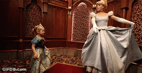 A Little Girl In A Dress Is Standing Next To A Cinderella GIF