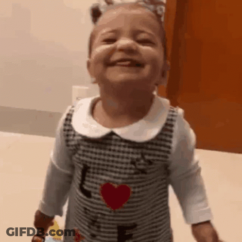 A Little Girl In A Dress With A Heart On It Is Smiling And Laughing . GIF
