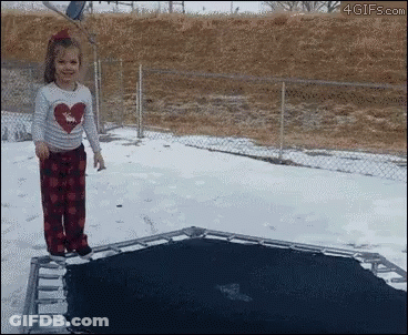 A Little Girl In A Heart Shirt Is Jumping On A Trampoline In The Snow GIF