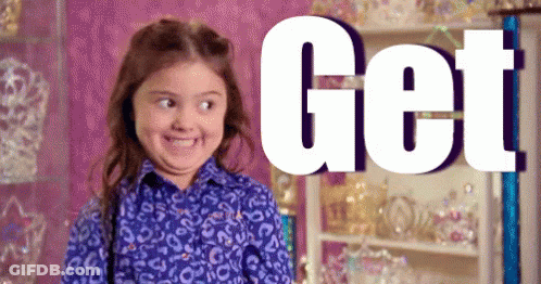 A Little Girl In A Leopard Print Shirt Is Smiling In Front Of A Sign That Says Get . GIF