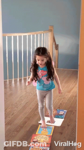 A Little Girl In A Peppa Pig Shirt Is Standing On A Stack Of Books On The Floor GIF