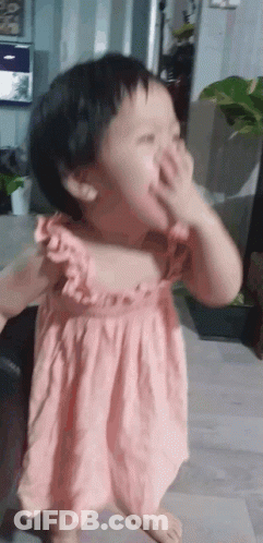 A Little Girl In A Pink Dress Covering Her Face With Her Hand GIF