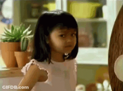 A Little Girl In A Pink Dress Is Standing In Front Of A Wooden Wall . GIF