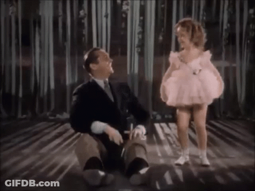 A Little Girl In A Pink Dress Is Standing Next To A Man In A Suit On A Stage . GIF