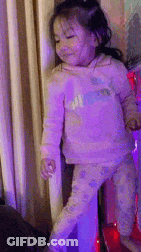 A Little Girl In A Pink Shirt And Pants Is Standing On A Red Carpet . GIF