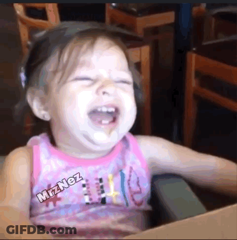 A Little Girl In A Pink Tank Top Is Laughing While Sitting At A Table . GIF