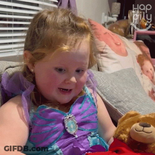 A Little Girl In A Purple And Blue Dress Holds A Teddy Bear GIF