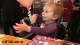 A Little Girl In A Purple Shirt Is Holding A Balloon In Her Hand GIF