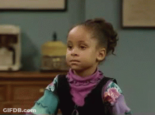 A Little Girl In A Purple Shirt Is Sitting At A Table Making A Funny Face . GIF