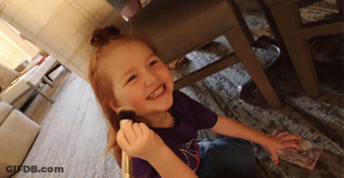 A Little Girl In A Purple Shirt Is Smiling While Holding A Brush In Her Hand GIF