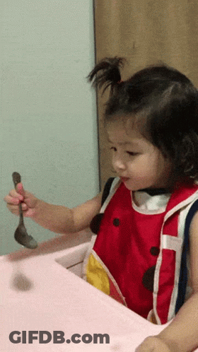 A Little Girl In A Red And White Bib Is Holding A Spoon GIF