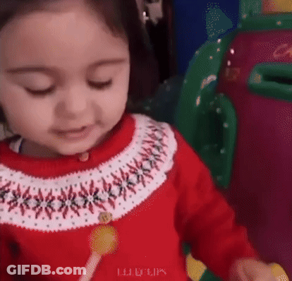 A Little Girl In A Red And White Sweater Is Holding A Lollipop . GIF