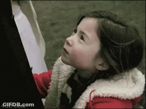 A Little Girl In A Red Jacket Is Looking Up At The Sky GIF