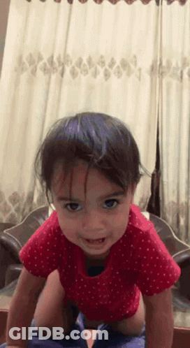 A Little Girl In A Red Polka Dot Shirt Is Crawling On The Floor GIF