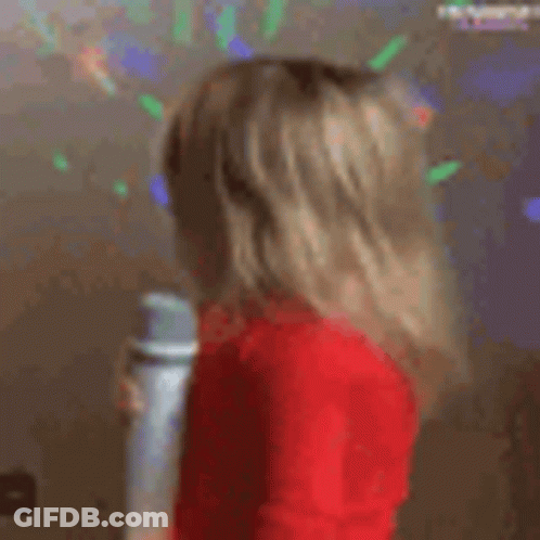 A Little Girl In A Red Sweater Is Holding A Microphone . GIF