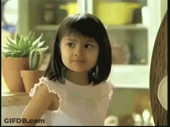 A Little Girl In A White Dress Is Standing In Front Of Potted Plants GIF