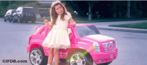 A Little Girl In A White Dress Sits In A Pink Toy Car GIF