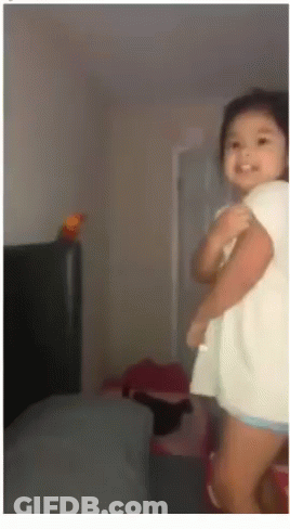 A Little Girl In A White Shirt Is Standing In A Room And Smiling GIF