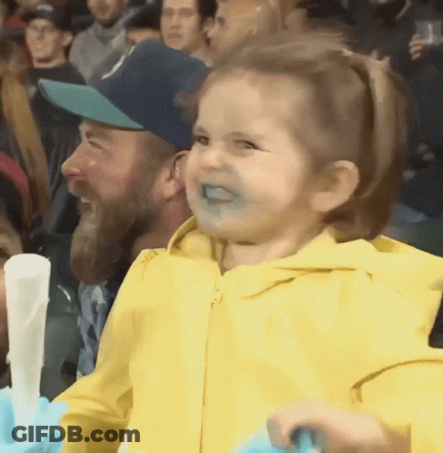 A Little Girl In A Yellow Jacket Is Making A Funny Face In A Crowd GIF