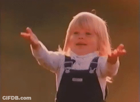 A Little Girl In Overalls Is Standing With Her Arms Outstretched In A Field . GIF
