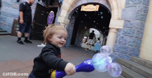 A Little Girl Is Blowing Soap Bubbles In Front Of A Building That Says Castle GIF