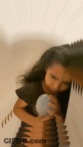A Little Girl Is Brushing Her Hair In Front Of A Mirror GIF