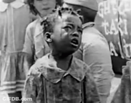 A Little Girl Is Crying In A Black And White Photo While Standing In Front Of A Sign . GIF