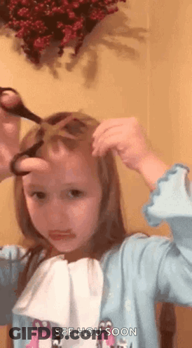 A Little Girl Is Cutting Her Hair With Scissors And Making A Face . GIF