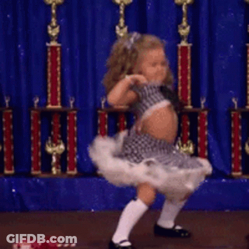 A Little Girl Is Dancing In Front Of Trophies And A Blue Curtain GIF
